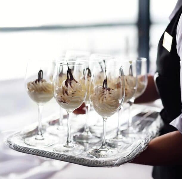 A server holds a tray filled with dessert glasses topped with whipped cream and chocolate drizzle.