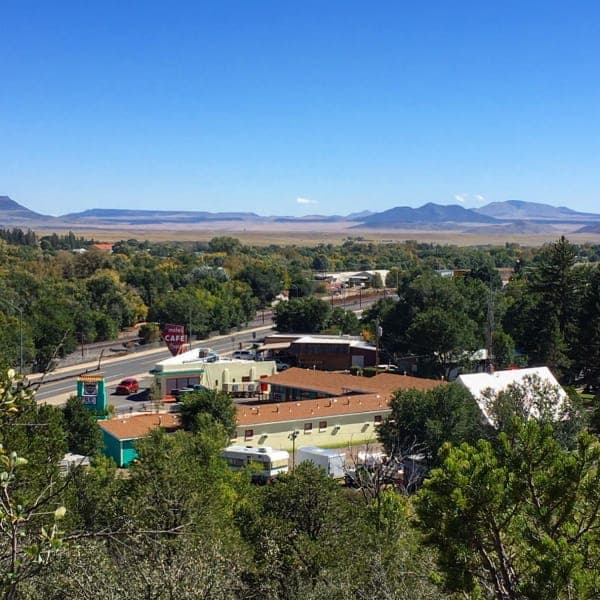 A panoramic view of a small town nestled among lush greenery with mountains in the background.