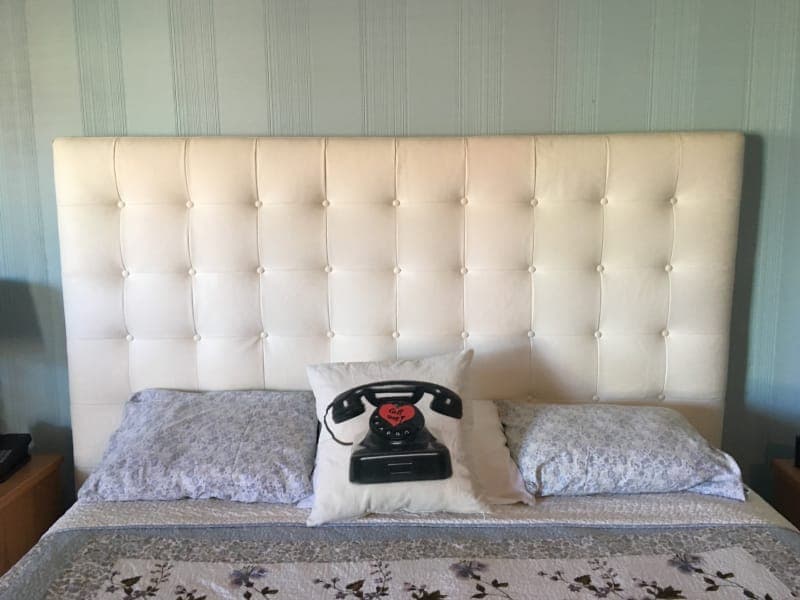 A stylish bed with a tufted white headboard, two patterned pillows, and a decorative pillow featuring a vintage telephone design.
