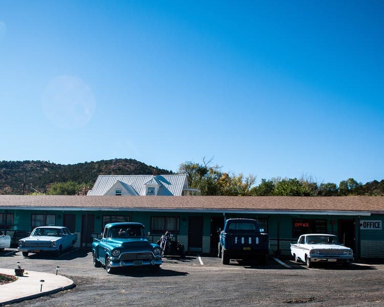 A vintage motel with retro cars parked in front under a clear blue sky.